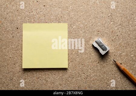 Bleistift-, Schärfer- und Papieraufkleber auf einer Spanplatte. Ansicht von oben. Stockfoto