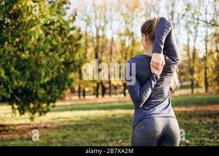 Schlankes Mädchen aus dem Rücken hält die Hände im Schloss und trainiert in der Natur. Stockfoto