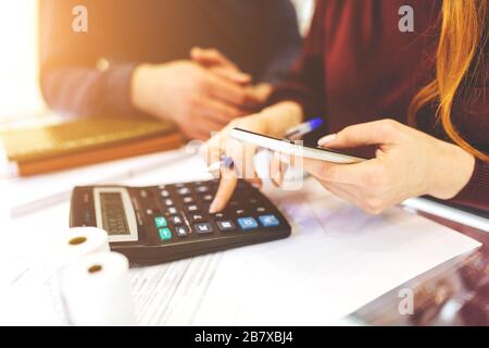 Frau und Mann arbeiten zu Hause, arbeiten zu Hause, mit Laptop und Notizblock, machen sich Notizen auf dem Telefon, zählt auf einem Rechner. Nahaufnahme von Buchhalterin oder Bankerin, die Berechnungen durchführt. Sparkonzept, Finanzen und Sparkonzept Stockfoto