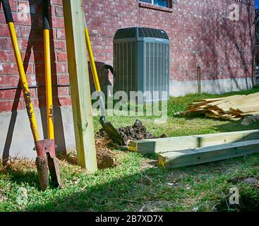 Neuen Zaun bauen. Hinterhof mit moderner Klimaanlage, Schaufeln und Schnittholz für neuen Zaun zum Schutz der Privatsphäre. Stockfoto