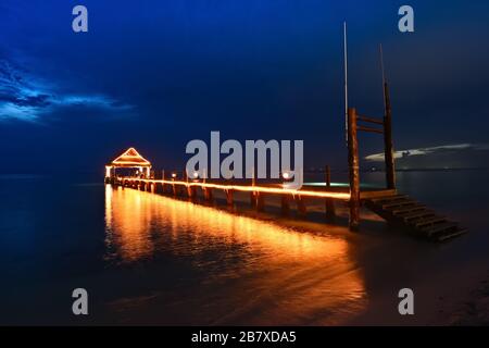 Tropisch-blauer dramatischer Sonnenuntergang mit bewölktem Himmel. Strahlendes Dämmerlicht des beleuchteten Piers am Strand von Cozumel Mexico Stockfoto