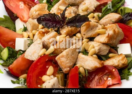Salat mit Huhn, Tomaten, Weichkäse, Käse und Grüns, mit Pinienknüssen dekoriert. mit Olivenöl kleiden. Nahaufnahme Stockfoto