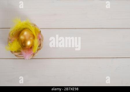 Hintergrund der Osterkarte. Ostergoldenes Ei auf weißem Grund in einem Federnest mit Kopierraum. Frohe ostern. Flaches Lay. Stockfoto