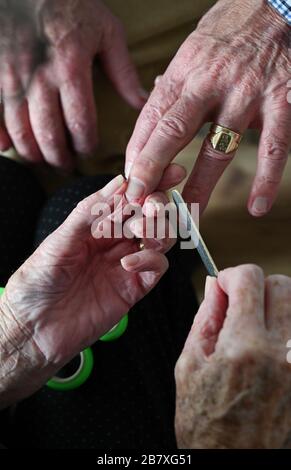 Ältere Paare in ihren Achtzigern schneiden sich zu Hause Fingernägel und verwenden Schmirgelbrett Stockfoto