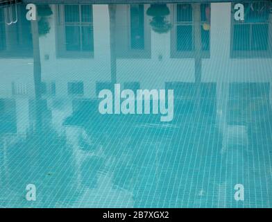 In einem blau gefliesten Wasserpool können Sie die Lichtreflexe von Häusern und Palmen beobachten. Stockfoto