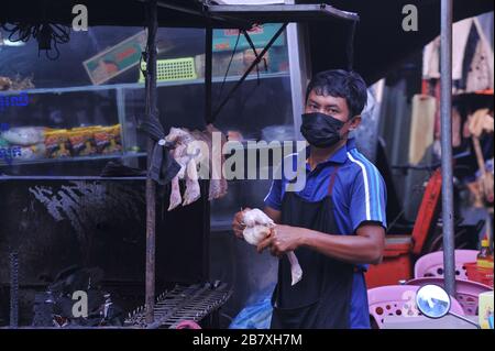 Ein kambodianischer Mann, der eine Gesichtsmaske trägt, verkauft gegrilltes Huhn auf dem Kandalmarkt während der Coronavirus-Pandemie. Phnom Penh, Kambodscha. © Kraig Lieb Stockfoto