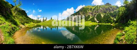 Wunderschöner See, umgeben von Bergen, mit tiefblauem, sonnigen Himmel und der atemberaubenden Landschaft, die sich im klaren Wasser widerspiegelt Stockfoto