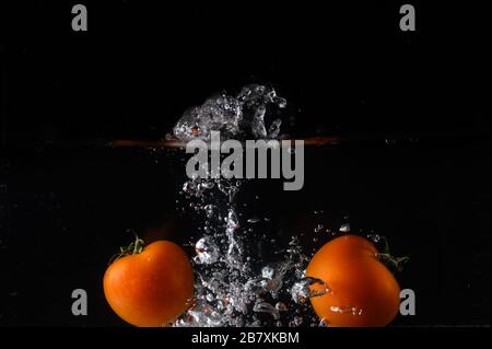 Isolierte Tomaten, die auf schwarzem Hintergrund in Wasser spritzen und Blasen erzeugen Stockfoto