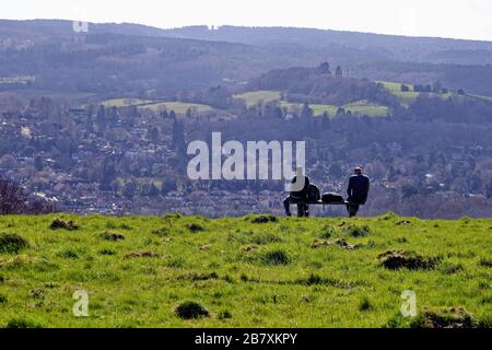 Zwei männliche Rammler, die auf einer Bank sitzen und die Ansicht von Westcott und Leith Hill an einem Frühlingstag von Ranmore Common, Surrey Hills Dorking England UK betrachten Stockfoto