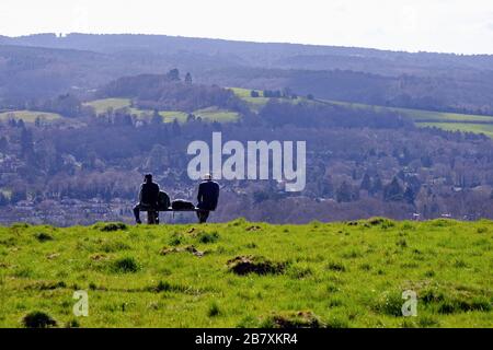 Zwei männliche Rammler, die auf einer Bank sitzen und die Ansicht von Westcott und Leith Hill an einem Frühlingstag von Ranmore Common, Surrey Hills Dorking England UK betrachten Stockfoto