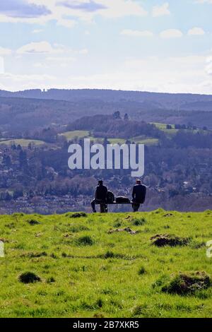 Zwei männliche Rammler, die auf einer Bank sitzen und die Ansicht von Westcott und Leith Hill an einem Frühlingstag von Ranmore Common, Surrey Hills Dorking England UK betrachten Stockfoto