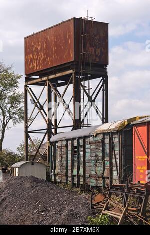Ein Metallwasserturm und alte Holzwagen im Güterhof von den Lokschuppen im Bahnhof Cranmore West der East Somerset Railway, England Stockfoto