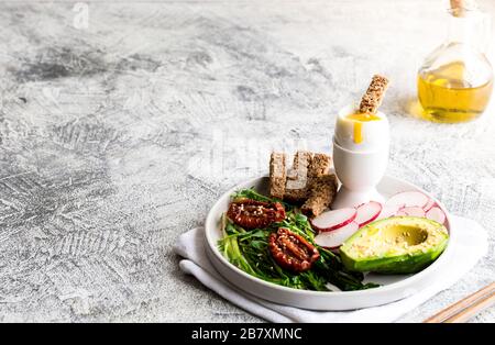 Nahrhaftes Frühstück. Wilder Knoblauch, sonnengetrocknete Tomaten, Vollkornbrot, Avocado, Samen und gekochtes Ei. Gutes Ernährungskonzept Stockfoto