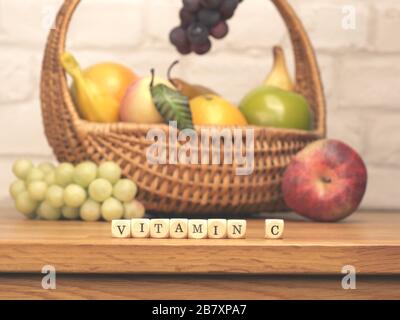 Kleine Holzblöcke mit den Worten Vitamin C auf einem Küchentisch mit frischen Früchten im Hintergrund, gesundes Lebensmittelkonzept Stockfoto