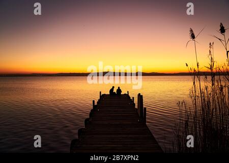 Ein Paar an einem Pier, das den Sonnenuntergang auf einem See beobachtet Stockfoto