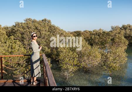 Weiblicher Tourist, der den Sonnenuntergang im Mangrove Walk Seaside Park in Abu Dhabi, VAE, genießt Stockfoto