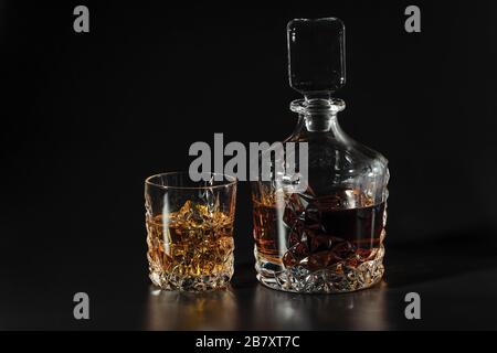 Whiskey-Dekanter mit schöner Aussicht und ein Glas Whisky mit Eis auf schwarzem Hintergrund. Schöne Hintergründe. A Stockfoto