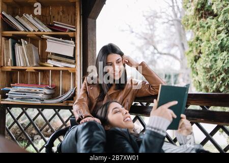 Lächelnde Frau, die ihrem weiblichen Freund Buch vorliest Stockfoto