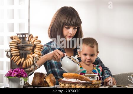 Die junge, niedliche Mutter gießt während einer Teeparty mit Gebäck Tee zu ihrem kleinen süßen Sohn. Das Konzept der traditionellen russischen Küche Stockfoto