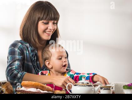 Die junge, niedliche Mutter gießt während einer Teeparty mit Gebäck Tee zu ihrem kleinen süßen Sohn. Das Konzept der traditionellen russischen Küche Stockfoto