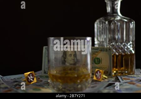 Karaffe mit Whisky und verstreute einhundert Dollar-Scheine auf den Tisch. Banknote glänzt durch ein Glas Whisky Stockfoto