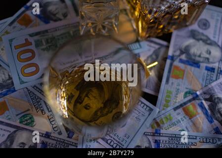 Dollar-Geld auf dem Tisch. Die 100-Dollar-Rechnung scheint durch den transparenten Boden eines Glases Whisky Stockfoto
