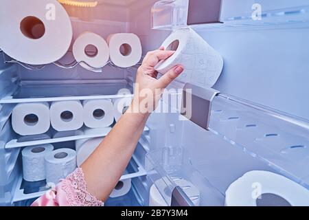Die weibliche Hand nimmt die Rolle von toilettenpapier von der Kühlschranktür. Panik beim Kauf von toilettenpapier in allen Ländern während der Verbreitung von COVID-19-Coronavirus und Quarantäne Stockfoto