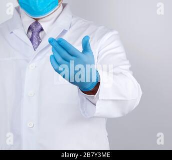 Doktor in einem weißen Mantel mit Knöpfen und blauen Latexhandschuhen hält seine Hand nach vorne, Einladungskonzept, Handschlag, weißer Hintergrund Stockfoto