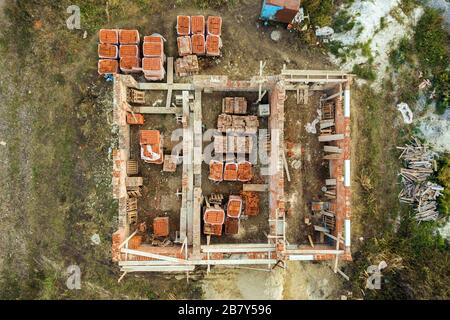 Luftbild der Baustelle für zukünftiges Ziegelhaus, Betonfundament und Stapel gelber Lehmziegel für den Bau. Stockfoto