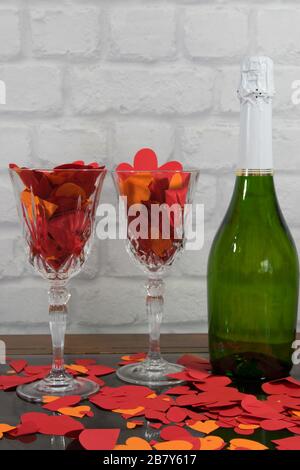 Rote Papierherzen und rotes Band auf den zwei Gläsern Champagner mit Flasche Champagner auf Steinstruktur Hintergrund mit Licht. Zeichen der Liebe. Stockfoto