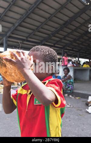 dh WEWAK PAPUA-NEUGUINEA Einheimischer kleiner Junge trinkt aus Kokosnuss PNG T-Shirt trinkt Kind Stockfoto