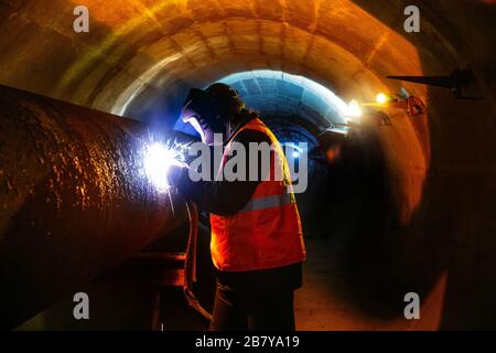 Arbeiter im Schutzmaskenschweißrohr im Tunnel Stockfoto