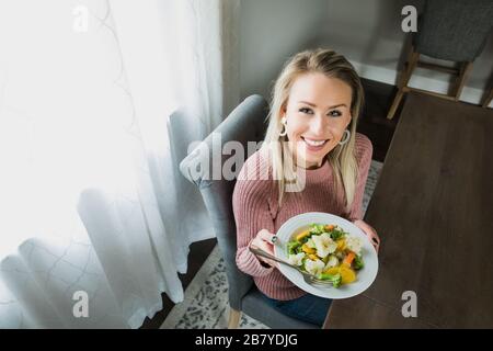 Eine junge und schöne Frau, die ihren Teller mit Gemüse zeigt Stockfoto