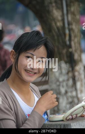 Guilin, China - 11. Mai 2010: Stadtzentrum. Junge Frau lächelt und macht ihr Make-up draußen entlang des Li-Flusses. Stockfoto