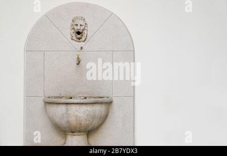 Altes Steinwaschbecken und ein kleiner Kran mit einem Löwen Skulptur darüber vor weißem Hintergrund Stockfoto