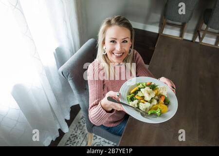 Eine junge und schöne Frau, die ihren Teller mit Gemüse zeigt Stockfoto