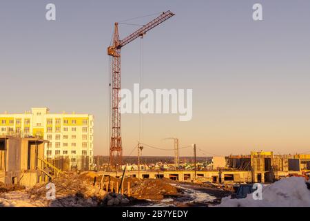 Am Frühlingsabend baut ein Turmkran am Stadtrand Gebäude, hebt und bewegt Waren vom und zum Boden Stockfoto