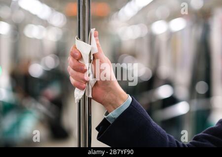 Nahaufnahme der Hand des Mannes hält einen Handlauf im öffentlichen Verkehr/U-Bahn durch eine Serviette, um sich vor dem Kontakt mit Viren, Keimen während eines coron zu schützen Stockfoto