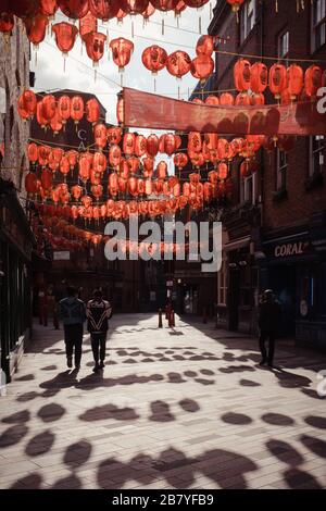 London, Großbritannien - 06. März 2020: Nur wenige Menschen laufen unter roten Laternen in weitgehend leerem Chinatown-Gebiet in London, das für seine Lokale und Veranstaltungen berühmt ist. Stockfoto