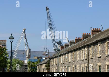 Hafenkräne über einer Reihe viktorianischer Terrassenhäuser, die für Dock- und Eisenbahnarbeiter im viktorianischen Industriedorf Greenore, Irland, gebaut wurden. Stockfoto