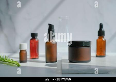 Set aus kosmetischen Hautpflegeverpackungen aus bernsteinfarbenem Glas. Beauty-Produkt auf luxuriösem weißem Marmor mit natürlichem Licht und Schatten verspotten. Stockfoto