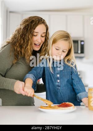 Frau, die mit ihrer Tochter Erdnussbutter und Gelee-Sandwich macht Stockfoto