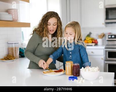 Frau, die mit ihrer Tochter Erdnussbutter und Gelee-Sandwich macht Stockfoto