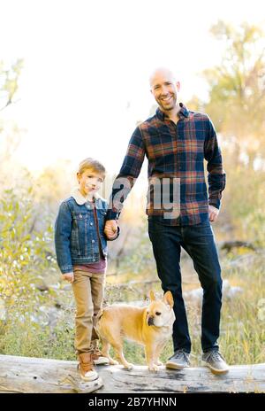 Vater und Sohn mit Haustier Französisch Bulldogge auf gefallenen Baum Stockfoto