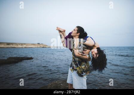 Junger Mann trägt Frau am Strand Stockfoto