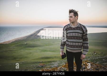 Junger Mann im gestreiften Pullover auf Hügel bei Sonnenuntergang Stockfoto