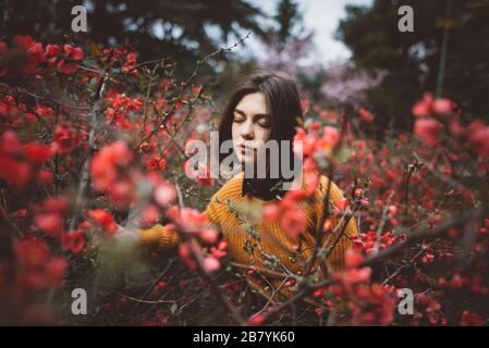 Junge Frau mit geschlossenen Augen in Sträuchern mit roten Blüten Stockfoto