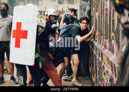 SANTIAGO, CHILE - 8. NOVEMBER 2019 - Freiwillige des Roten Kreuzes schützen während der Proteste-ag Zivilisten vor Polizisten und Projektilen von Demonstranten Stockfoto