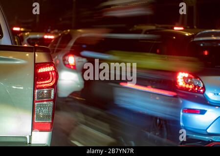 Ein verschwommenes Motorrad übertrifft im Stau eine Warteschlange von Autos. Abendverkehr auf den Straßen der Stadt, Bangkok, Thailand. Stockfoto