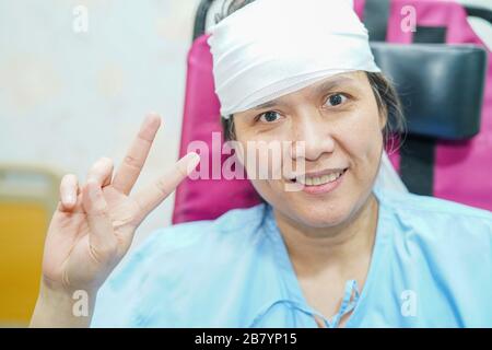 Asiatische Patientin im mittleren Alter, die auf dem Rollstuhl sitzt, mit einem fröhlichen und hellen Gesicht in der Krankenstation: Gesundes medizinisches Konzept Stockfoto